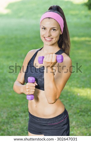 Fitness Slim Woman Training with dumbbells. Smiling attractive female practicing using hand weights outdoor. Healthy lifestyle workout concept on beautiful summer day.
