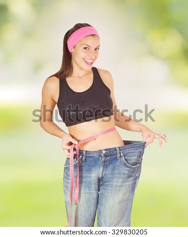Slim Female with perfect healthy fitness body, measuring her thin waist with a tape measure. Caucasian young woman in jeans ,over nature background. Diet and weight loss concept.