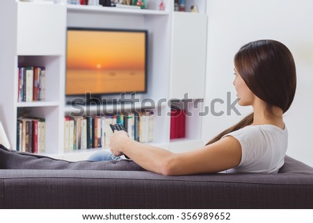 Young woman with remote control, watching TV program at home,Photo on television is from my gallery.