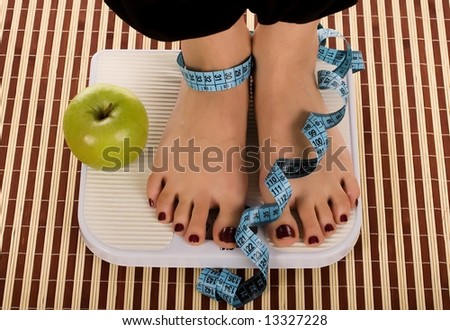 Woman foot on measuring scale with tape and apple.