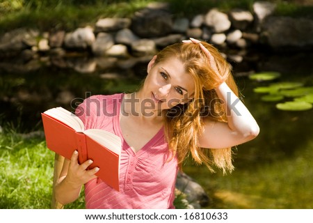 Beautiful young student reading book in natural environment.