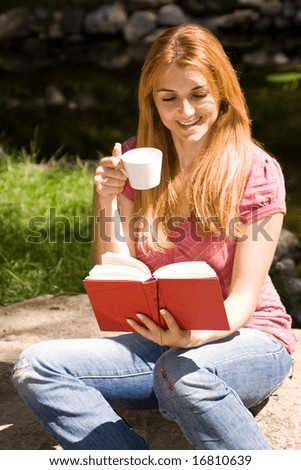Beautiful young student reading book and drink coffee in natural environment.