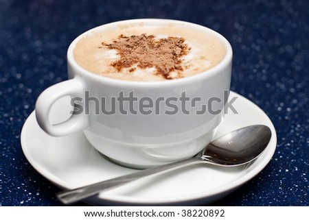 Cup of cappuccino with spoon on blue background.