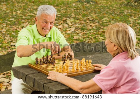 Happy senior couple playing chess on a park bench.
