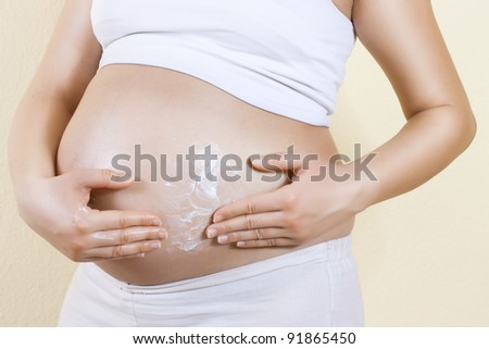 Pregnant woman applying cream to her belly.