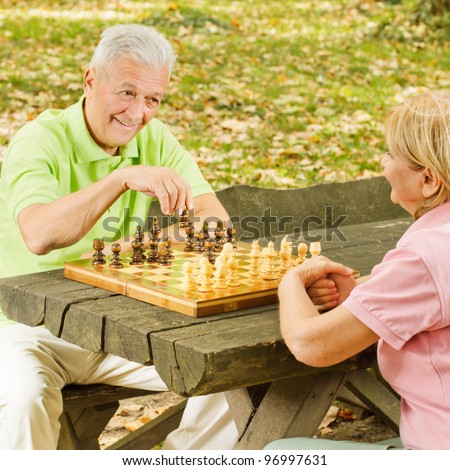 Happy elderly couple has fun playing chess in the park.