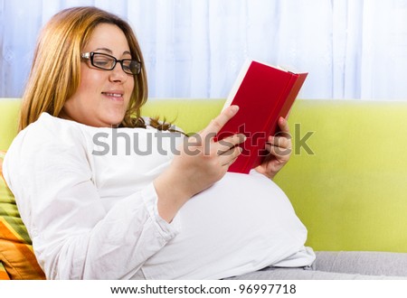Portrait of happy pregnant woman reading a book in the home environment
