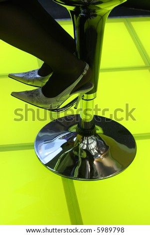 Bar stool and woman\'s feet in high-heeled shoes