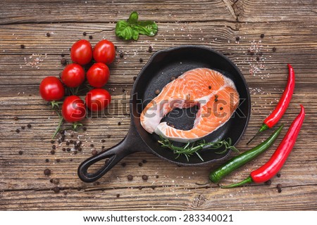 Salmon steak in pan and vegetables on old wooden background. Top view. Toned