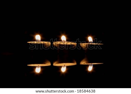 Row of three candles with their reflection