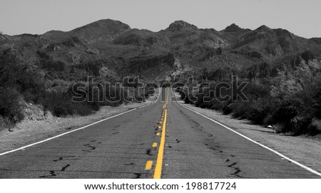 Black and white long lonely road with colorful yellow strip and mountains in background