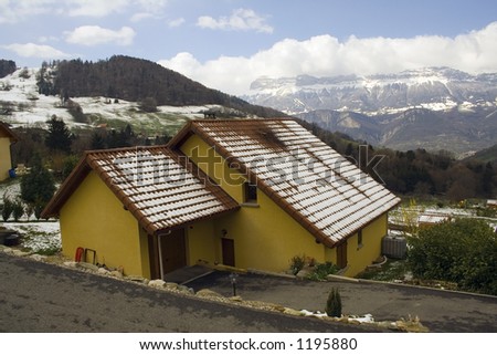 Lovely house  with fresh snow on the roof, with snowy mountains on the background