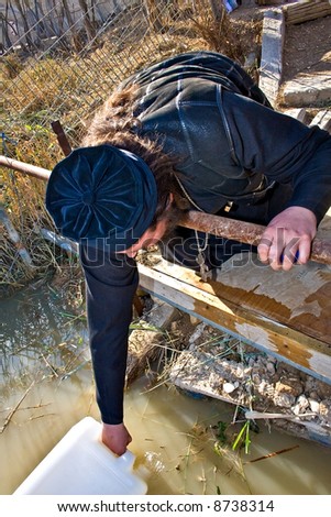 Orthodox Christian filling a bottle with Jordan river Holy Water, Jesus Baptism site, Israel