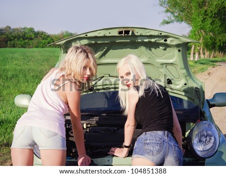 Two sexy blonde girls stand by the broken car and don\'t know what to do. Rear view