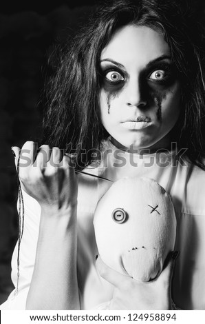Horror scene: strange crazy girl with moppet doll and needle in hands. Closeup, black and white