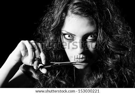 Horror shot: scary strange girl with mouth sewn shut cutting off the thread. Monochrome