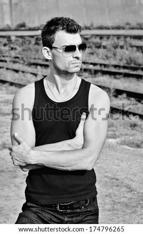 Fashion shot: portrait of a handsome young man in black shirt wearing sunglasses. Black and white