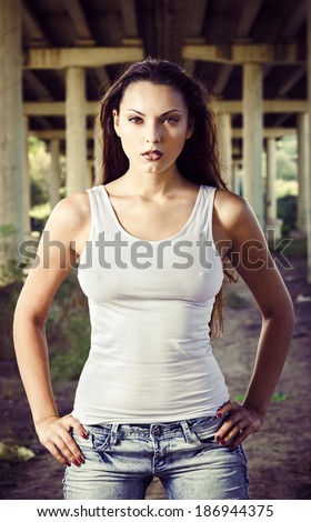 Beautiful young woman in shirt and jeans stands under the bridge
