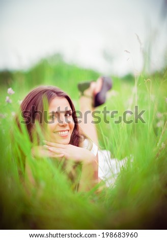 Happy smiling beautiful young woman lying among the grass and flowers