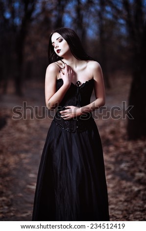 A beautiful sad goth girl stands in a grove