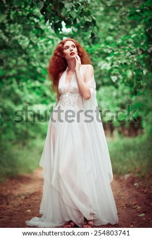 Beautiful redhead woman wearing white dress, in the forest