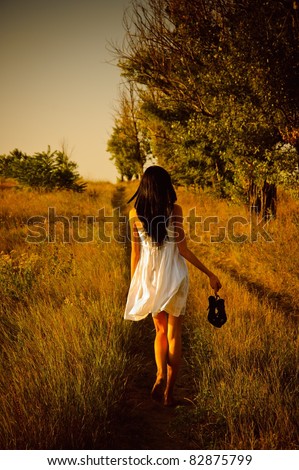 stock photo The barefoot girl in white dress with shoes in hand is on the