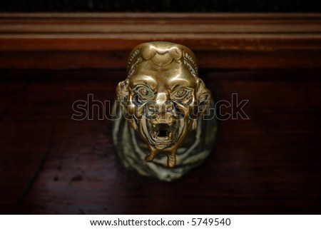 Creepy head shaped brass doorknob on dark wooden door in Venice, Italy. Face on doorknob looks slightly monstrous.