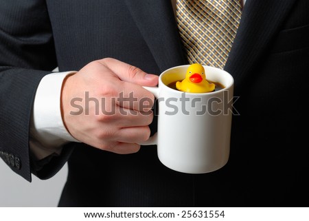 Yellow rubber ducky floating in a coffee cup being held by a man in a business suit.