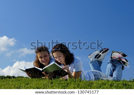 Two happy girls reading books in the nature studying outside in a park lying on green grass
