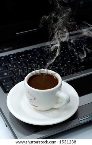 Cup of hot black steaming coffee on a laptop computer business office environment concept still-life background