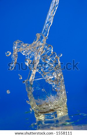 Water splashing over the top of the glass dynamic motion on blue background