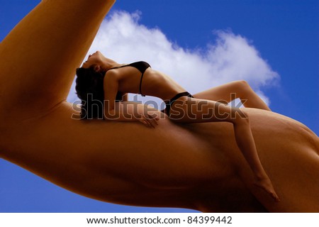 Beautiful young woman in bikini resting on a man\'s biceps. Fitness, tanning, health and beauty concept.