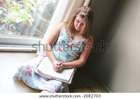 A teenage girl praying while sitting by the big window