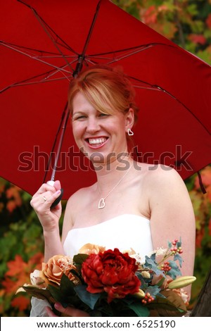 Happy bride laughing about the rain on her wedding day. She is holding a big red umbrella