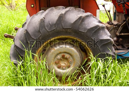 Old farm tractor in long grass with broken tires and rusty