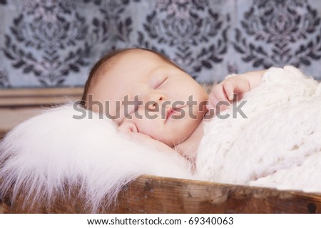 Sleeping infant in vintage crate with damask wallpaper
