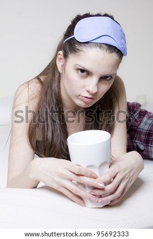 Young woman in the bed, with a cup of tea and blinkers in her head