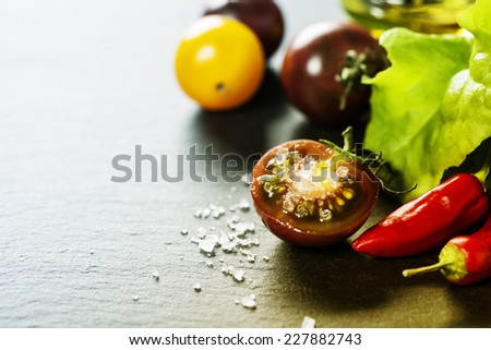Fresh grape tomatoes with salade leaves and salt for use as cooking ingredients with a halved tomato in the foreground with copyspace