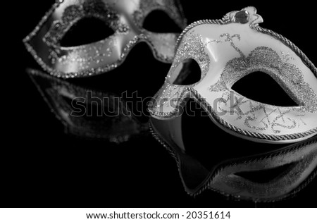 Carnival masks on a black background. The part of masks is reflected by the glass surface. Black and white image