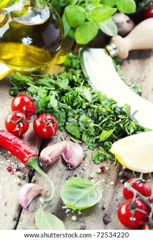 fresh and chopped herbs on cutting board with a mezzaluna, olive oil and vegetables