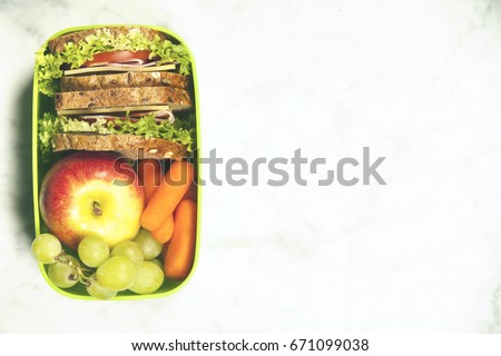 Green school lunch box with sandwich, apple, grape and carrot close up on white background. Healthy eating habits concept. Flat lay composition (from above, top view).