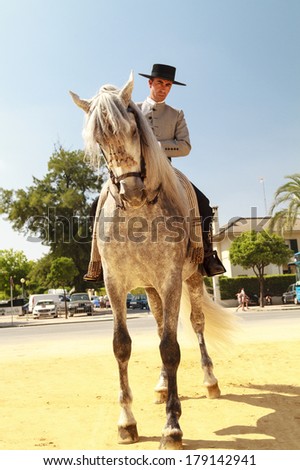 JEREZ DE LA FRONTERA, SPAIN-MAY 12 2013: Male rider decked out in flat-topped hat on his noble horse in the sandy street of Jerez during Feria del Caballon, Spains horse fair that lasts for 3 weeks.