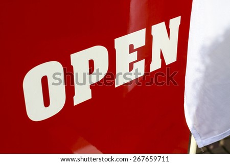 Big red and white sign saying open next to a white cloth flag