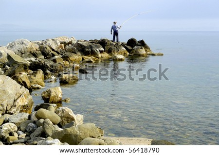 Old greek fisherman on the rocks fishing in the sea