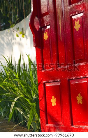 Bright red painted wooden door leading to a lush tropical garden