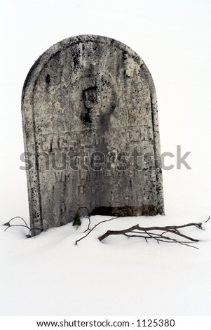 An old headstone blanketed with snow with a bare branch reaching out from under