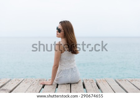 Young pretty woman sitting alone on the pier near the sea and looking on the water and waiting for somebody in ocean