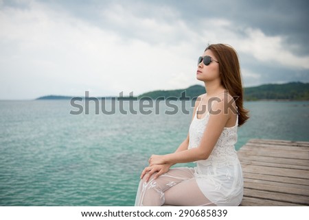 Young pretty woman sitting alone on the pier near the sea