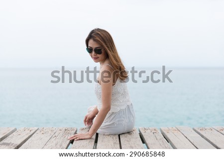 Young pretty woman sitting alone on the pier near the sea