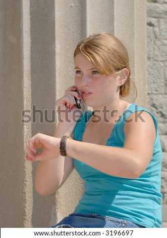 Impatient girl, sitting outside, looking at her watch and talking on her cell phone